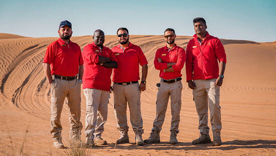 Five Arabian Adventures team members posing for a photo in the desert