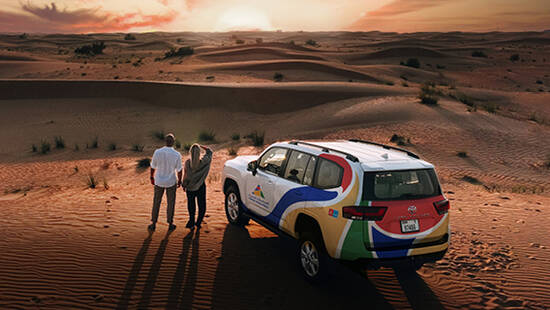 Two people watching the sunset in the desert next to an Arabian Adventures 4x4