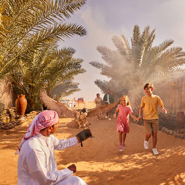 Kids at a desert camp in Dubai running towards a man dressed up in an Emirati outfit holding up an eagle