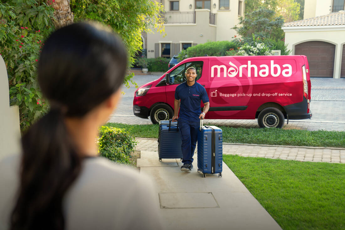 A marhaba team member walking up a garden path, away from a marhaba branded van, with two suitcases