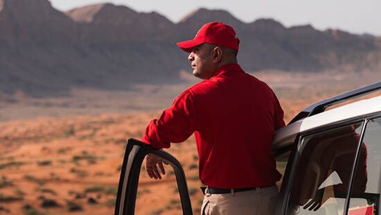 An Arabian Adventure representative looking at a vehicle driving down a sand dune