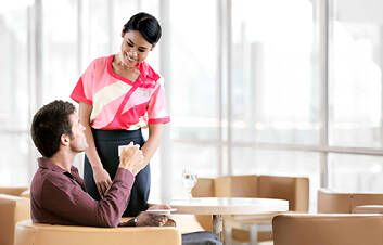 A man sitting in an airport lounge and drinking from a mug while speaking to a marhaba representative 
