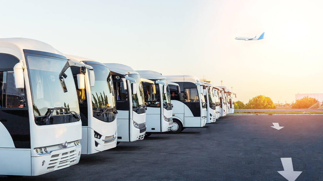 Buses lined up at the terminal with an aircraft flying in the background