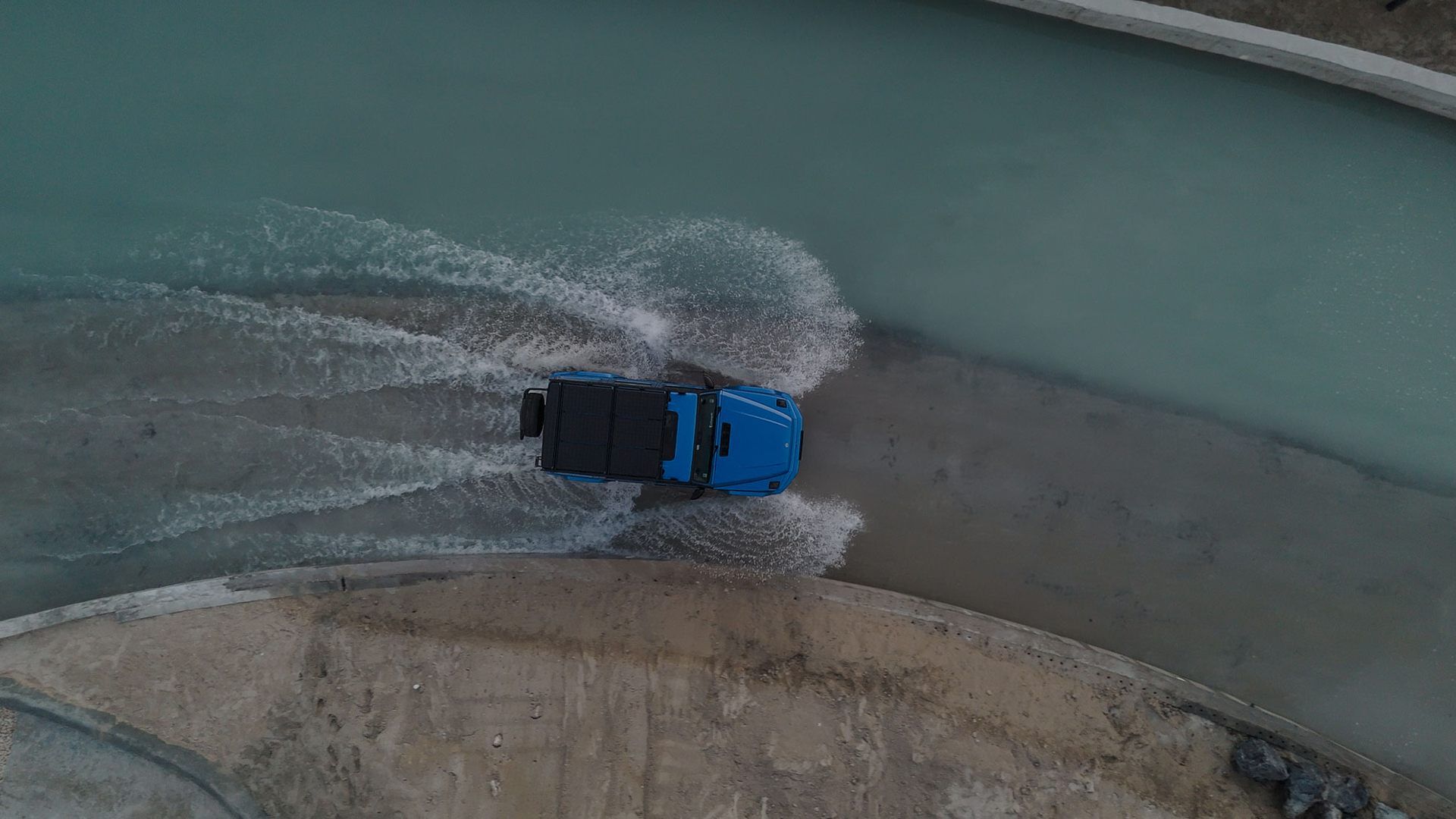A blue Mercedes Benz driving through a watery road