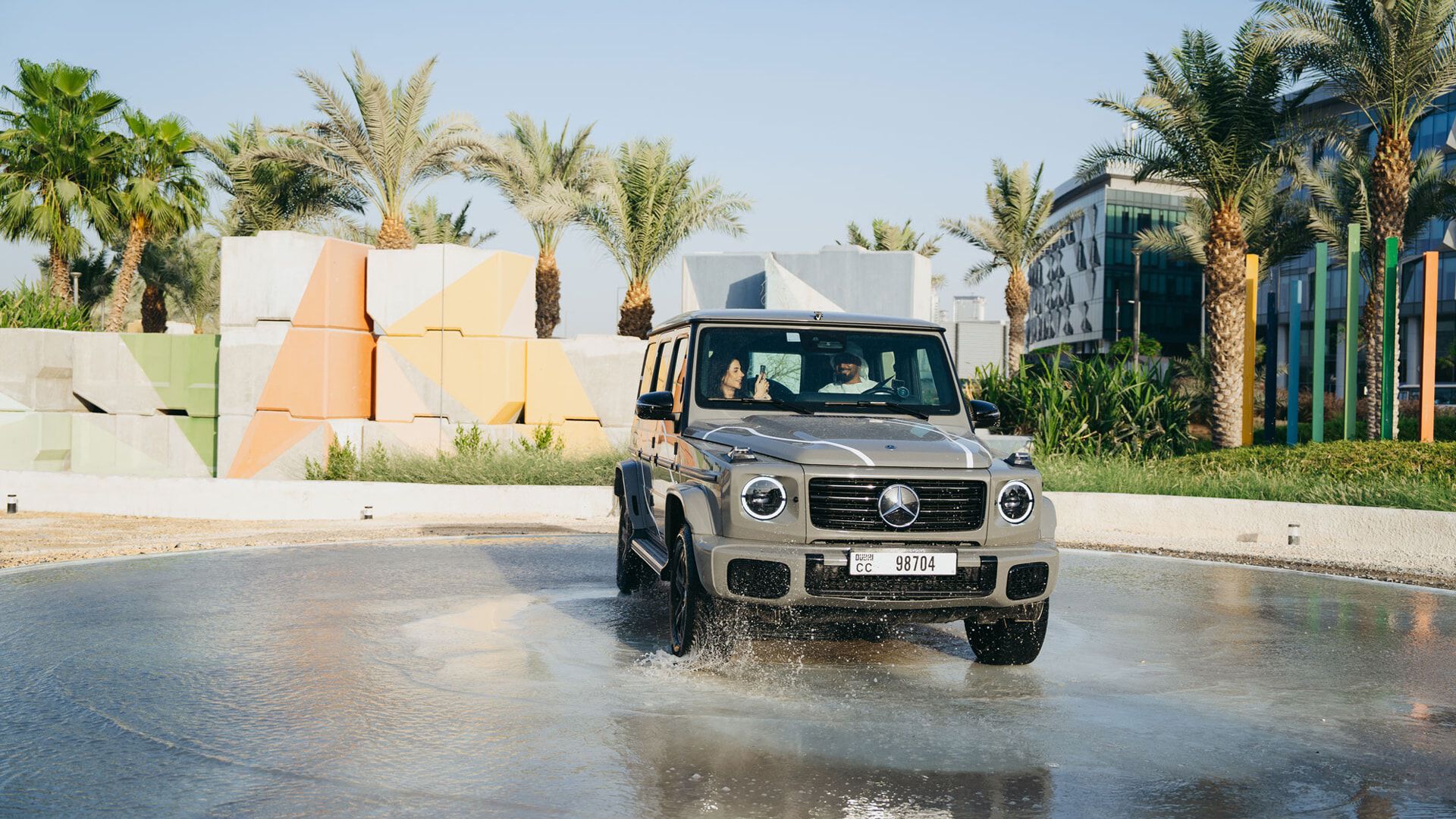 A lady and man inside a grey G-Class driving through a water puddle