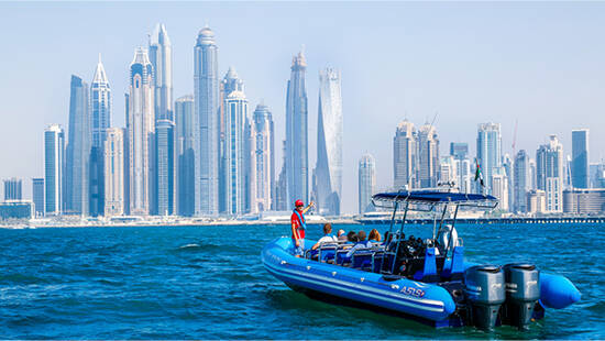 A guide with a group of tourists on a blue boat pointing at the Dubai Skyline from the sea