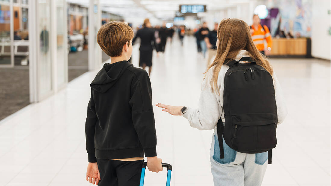 A boy and a girl holding luggage and walking through an Airport