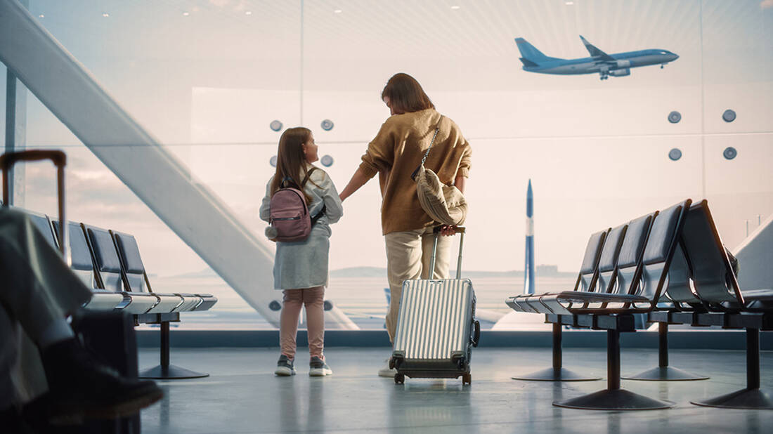 A mother and daughter looking at a plane flying above the runway from the airport