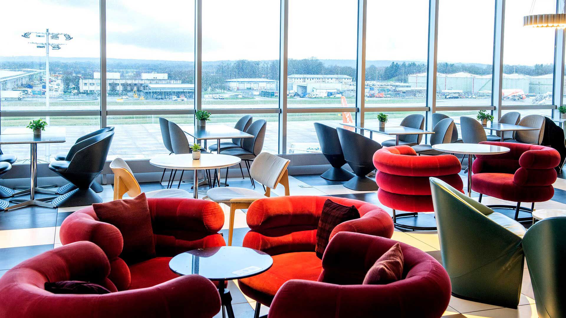 Image of the red armchairs seating area and navy blue dining area inside the Plaza Premium Lounge London Gatwick Airport overlooking the airport runway