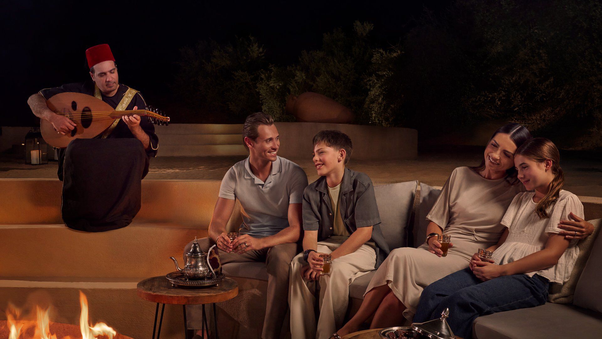 A family seated in sunken fire pit with oud player playing the oud